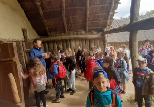 Uczniowie z przewodnikiem zwiedzają chatę w osadzie w Biskupinie
